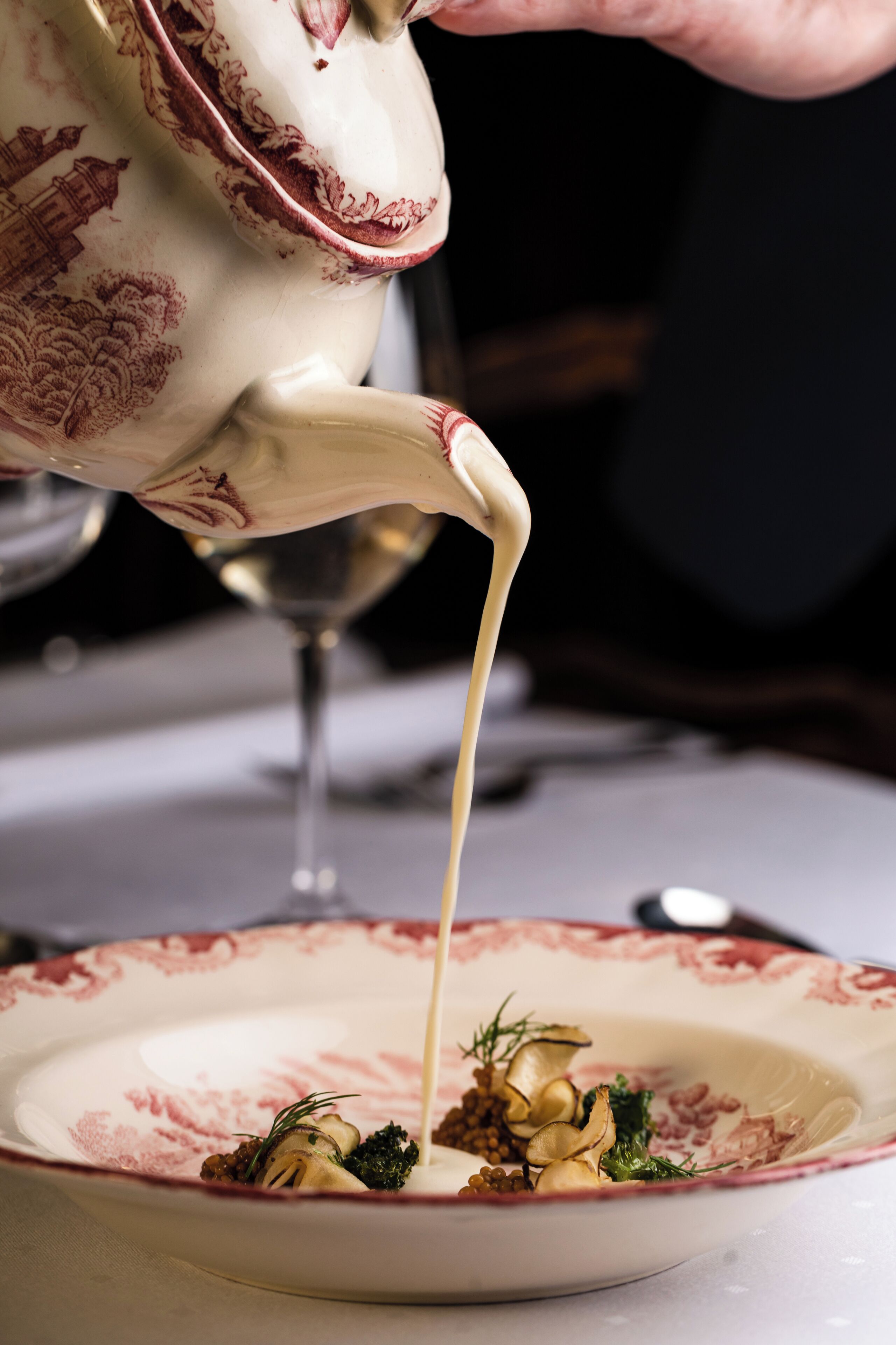 A teapot pouring cream into a plate with food.