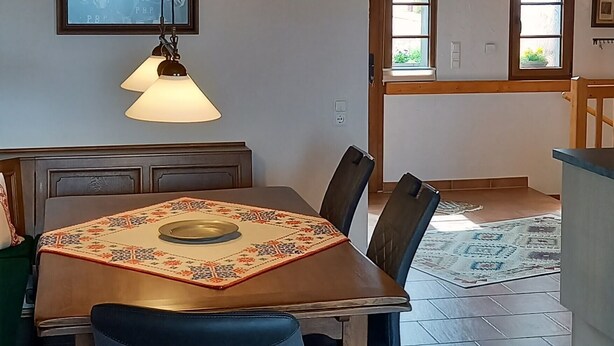 Een eetruimte met een houten plafond, een tafel met een tafelkleed met patroon, en blauwe gestoffeerde stoelen.
