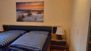 Een slaapkamer met twee bedden, een schilderij van een zonsondergang en een nachtkastje met een lamp.