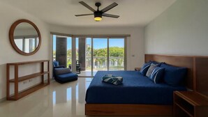A bedroom with a large bed, a ceiling fan, a round mirror, and a view of the outdoors through a sliding door.