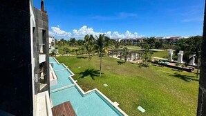 A hotel with a swimming pool, a grassy lawn, and a clear blue sky.