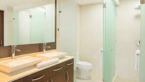 A modern bathroom with a large mirror, two sinks, a toilet, and a glass-enclosed shower area.