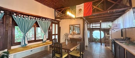 Un comedor con una mesa y sillas de madera, un banco junto a la ventana y vistas al exterior.