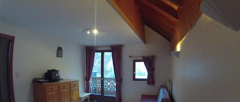 Uma área de refeições com mesa e bancos de madeira, um armário de madeira e uma janela com cortinas.