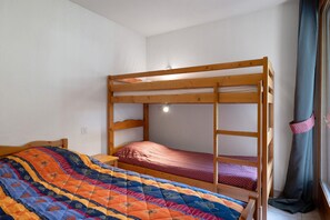 A bunk bed with a colorful quilt, a wooden headboard, and a window with curtains. - Apartment 'Les Roches' with Mountain View (Saint-Colomban-des-Villards)