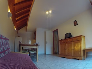 A bedroom with a bed, a wooden cabinet, a television, and a kitchen area with a refrigerator and a table. - Apartment 'Les Roches' with Mountain View (Saint-Colomban-des-Villards)