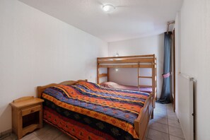 Un dormitorio con una litera, una mesita de noche de madera, un edredón colorido y una ventana con cortinas.