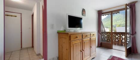 A room with a wooden cabinet, a television, and a balcony with a view of a mountainous landscape.