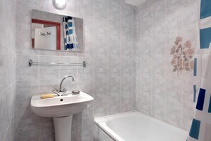 Une salle de bain avec un lavabo blanc, un miroir et une baignoire.