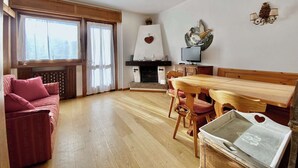 A cozy living room with a wooden dining table, chairs, a sofa, and a fireplace. - Cozy 3 bedroom in amazing location (Cortina d'Ampezzo)