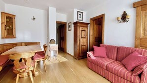 A cozy living room with a wooden dining table, chairs, a patterned sofa, and a wooden wardrobe. - Cozy 3 bedroom in amazing location (Cortina d'Ampezzo)