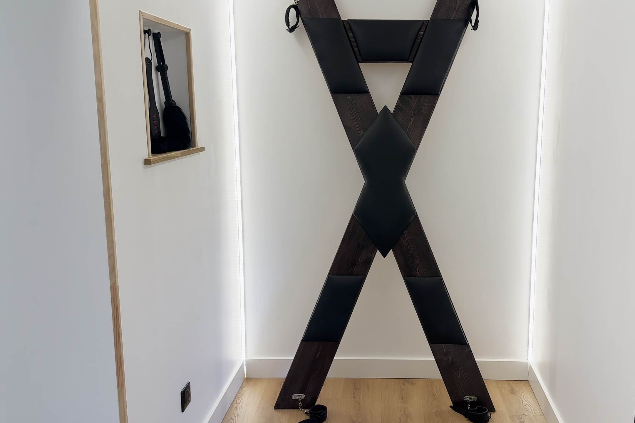 Une pièce avec un plancher en bois, des murs blancs et une structure noire en forme de X.
