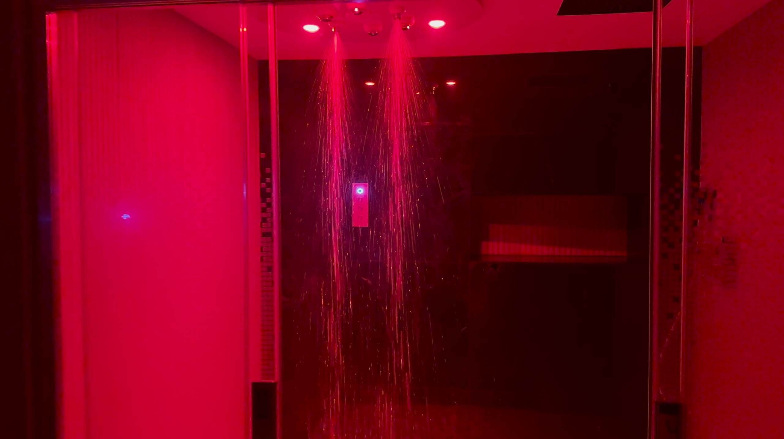 Een kamer met een douchegedeelte dat rood verlicht is en een zichtbaar bedieningspaneel.