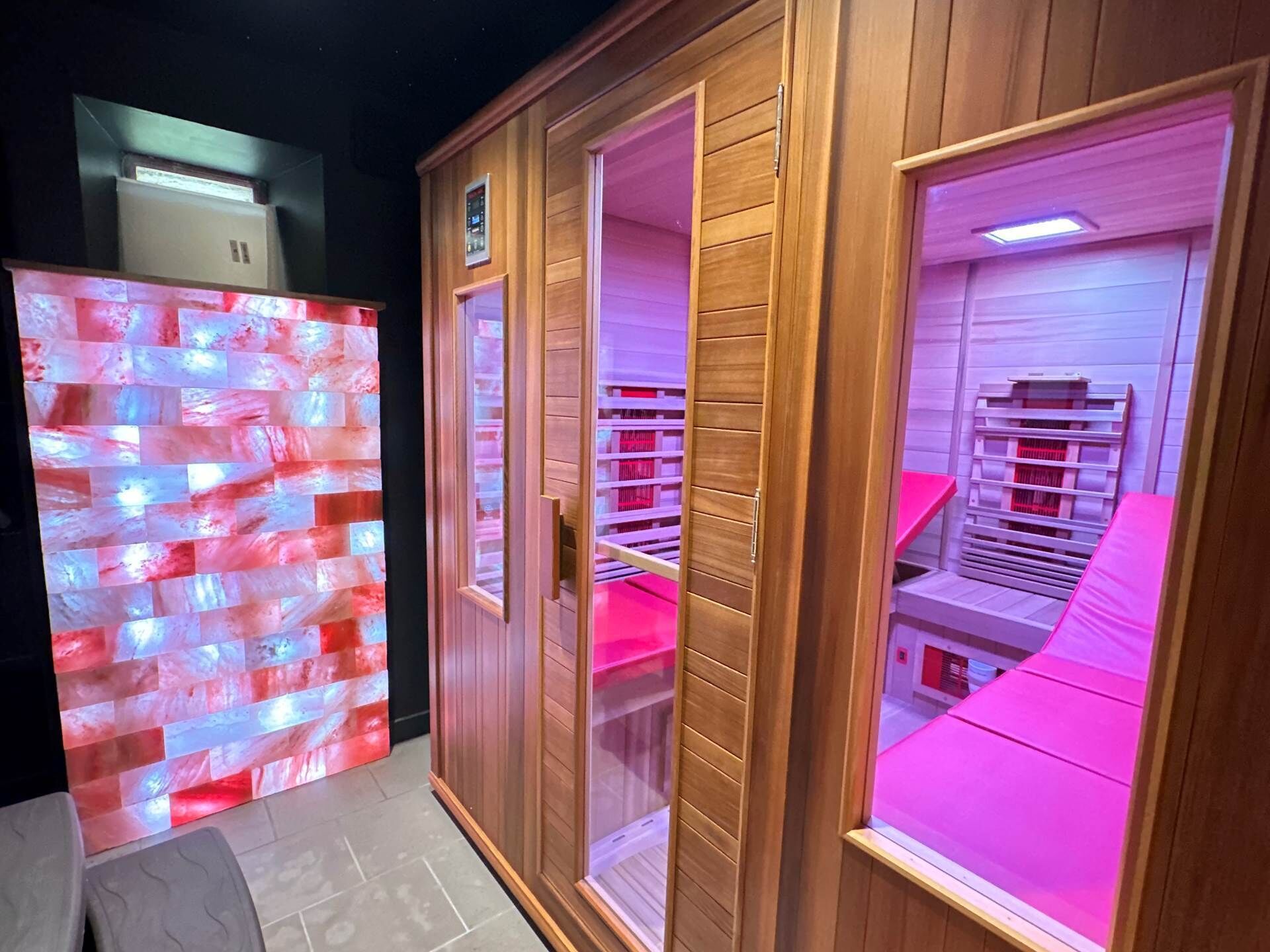 A room with a wooden wardrobe, a mirrored wardrobe, and a pink-lit vanity.