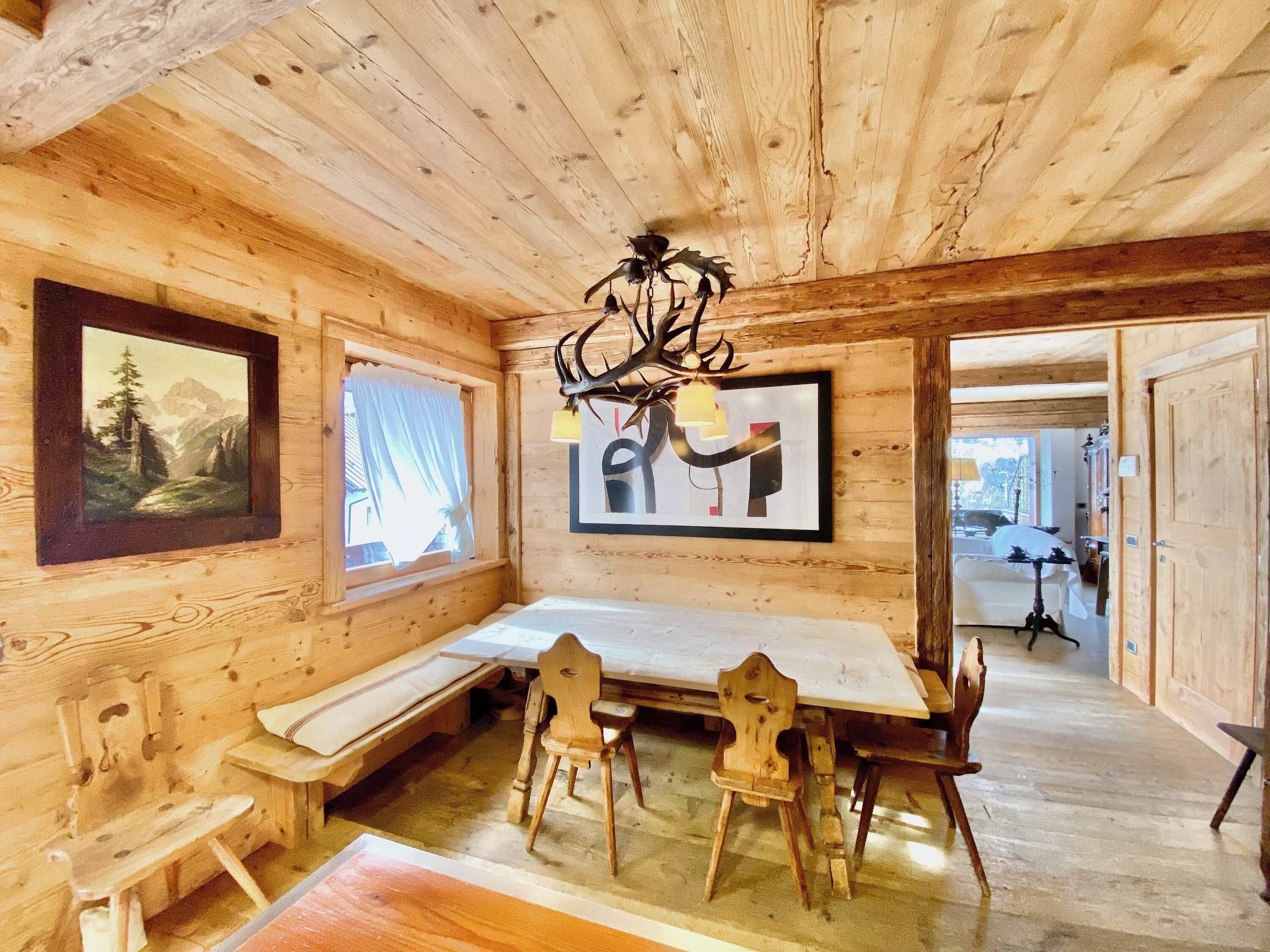 A wooden interior with a dining table, benches, and artwork on the walls.