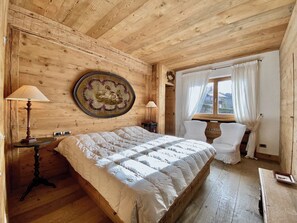 Ein Zimmer mit Holzboden, einem Bett, zwei Nachttischen, einer Lampe, einem Fenster mit Vorhängen und einem Wandbild.
