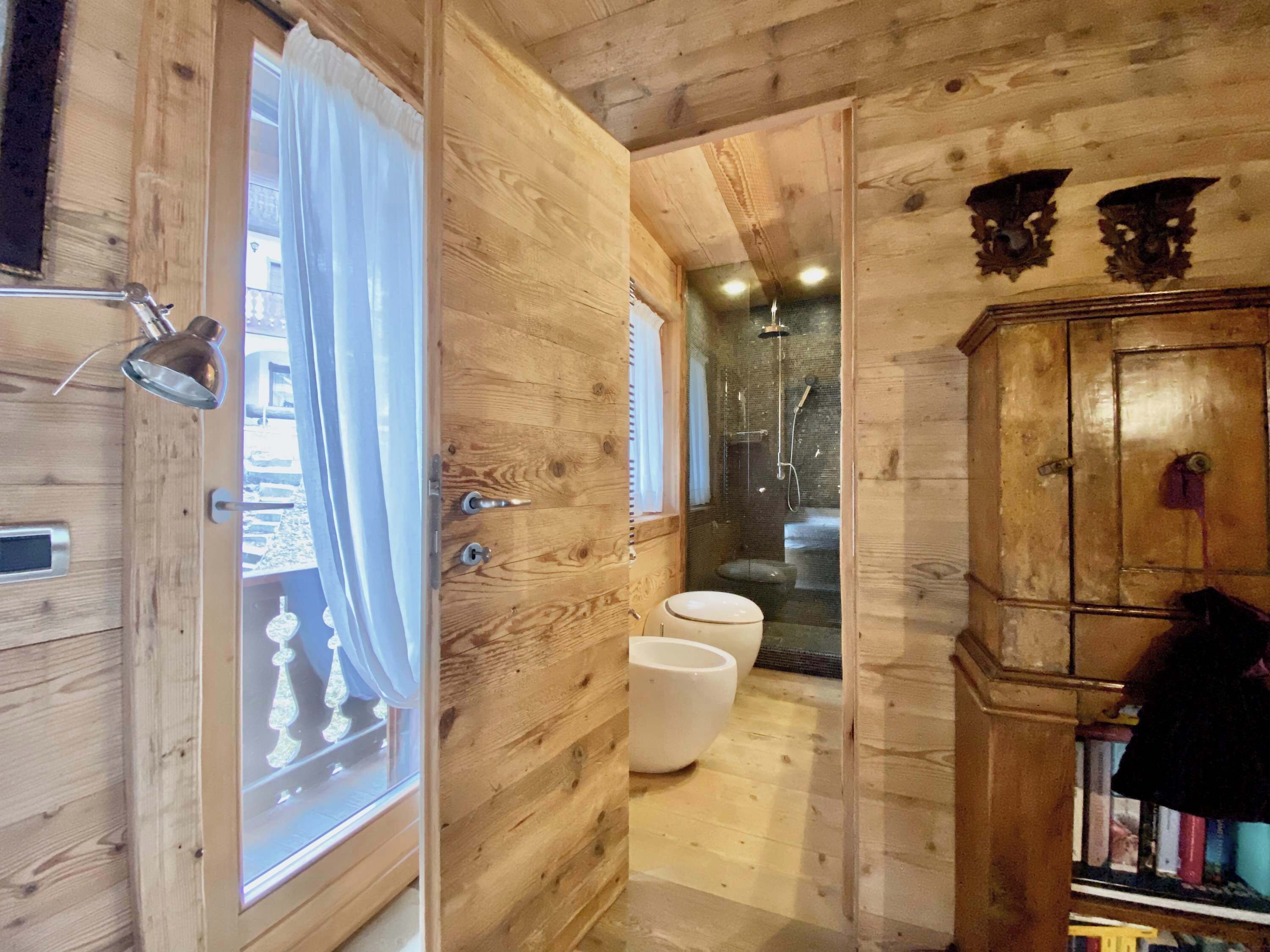 Un intérieur en bois avec une porte en bois, une fenêtre avec des rideaux, un espace douche et un meuble contenant des livres.