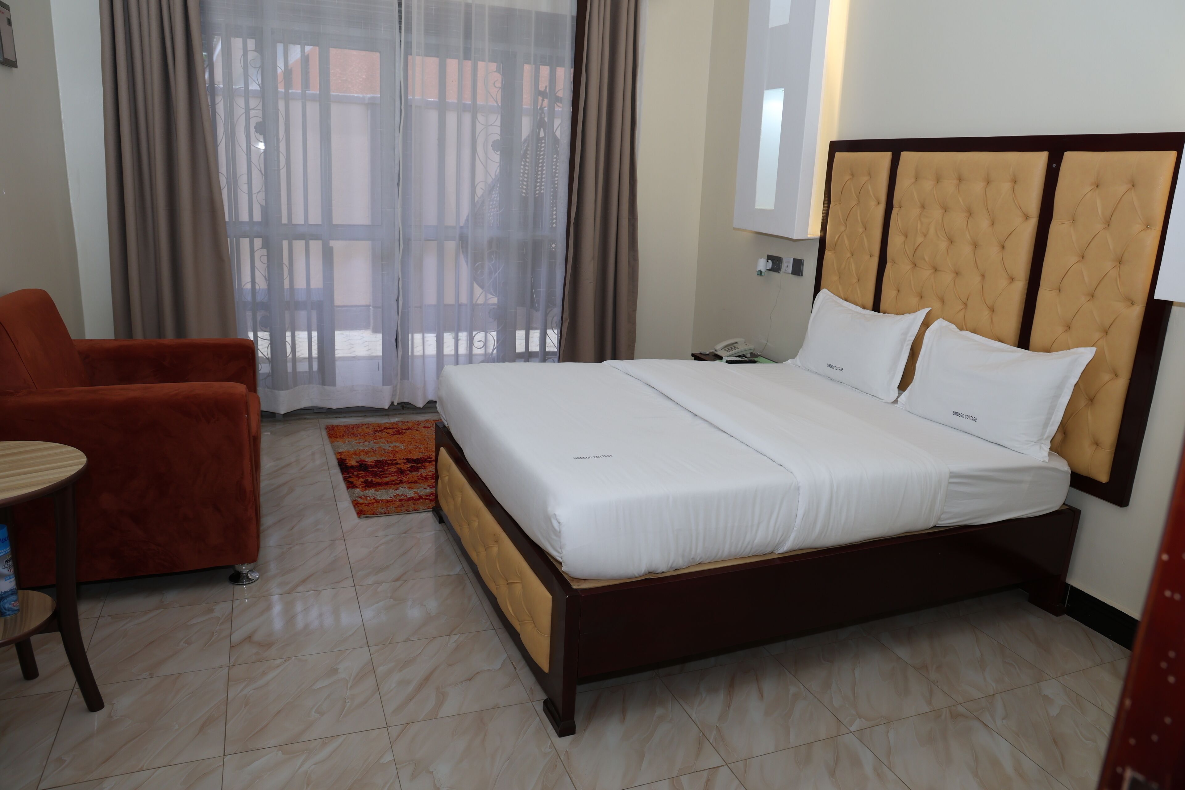 Quarto de hotel com cama, uma cadeira, uma mesa e vista pela janela com cortinas.