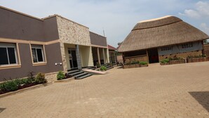 A building with a modern facade, a thatched-roof structure, and a paved courtyard. - Simbego Cottages  (Lira)
