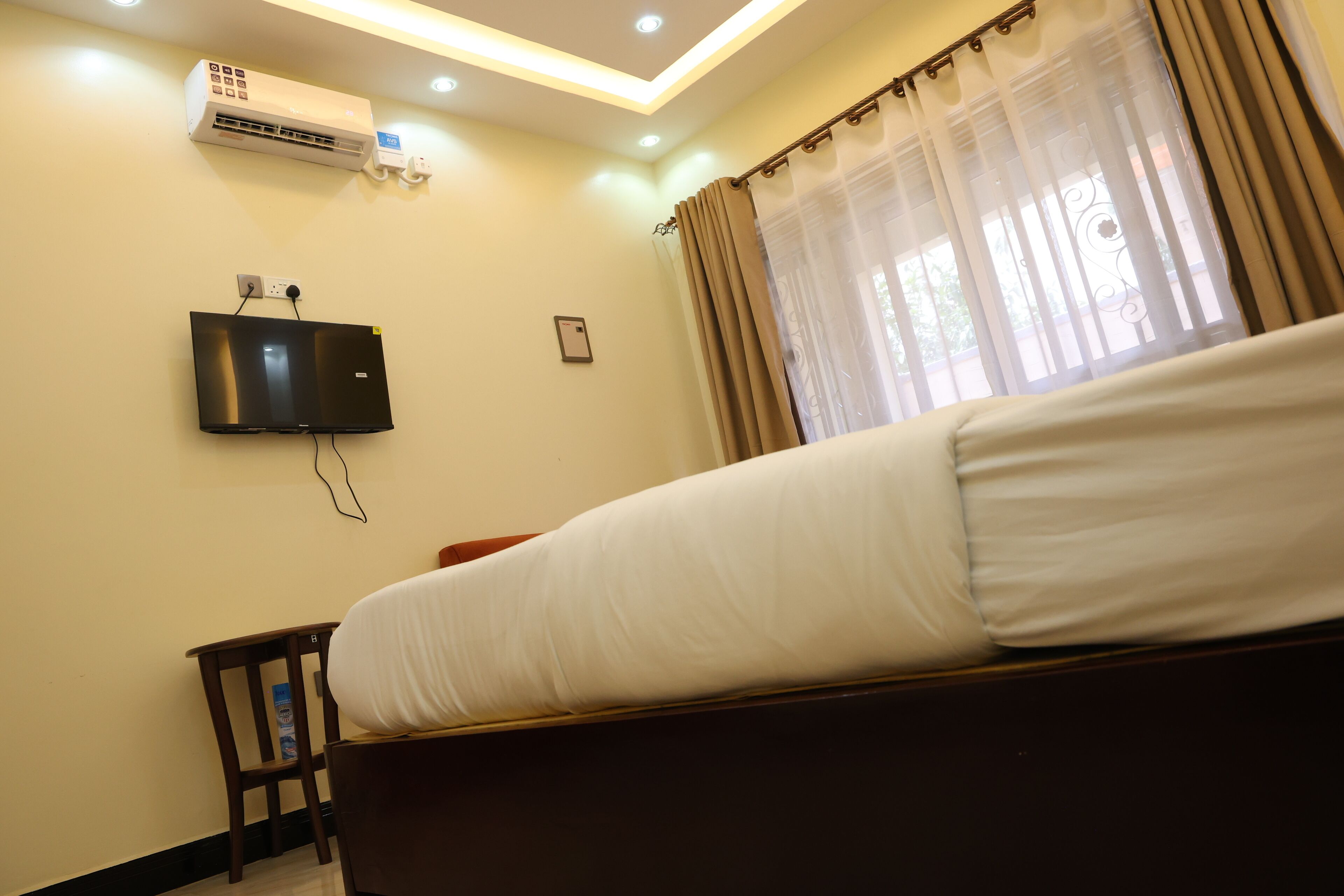 Une chambre d’hôtel équipée d’un lit, d’un téléviseur fixé au mur, d’un appareil de climatisation et d’une fenêtre avec des rideaux.