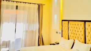 A hotel room with a large bed, a bedside table, and a window with curtains. - Simbego Cottages  (Lira)