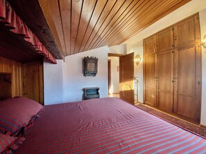 Ein Schlafzimmer mit Holzboden, einem großen Kleiderschrank, einem Bett mit rot-blau gestreifter Bettdecke und einer kleinen Holzkabine.