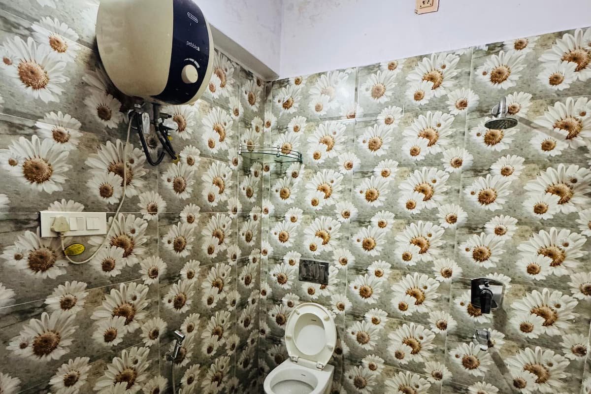 Un baño con inodoro, ducha y secamanos. Las paredes están decoradas con un estampado floral.