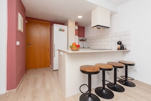 Cucina con una porta in legno, un frigorifero bianco, zoccolo di piastrelle bianche e tre sgabelli da bar in legno.