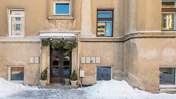 Um edifício com entrada coberta de neve, porta dupla escura e pequenos vasos de plantas nos degraus.