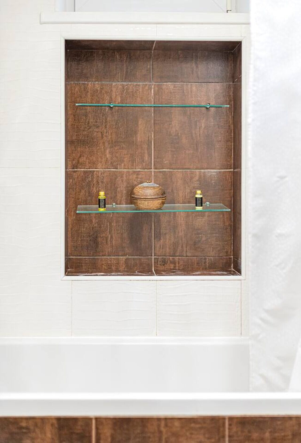 Ein Badezimmer mit einem Holzbadschrank, zwei Glasregalen und einer weiß gefliesten Wand.