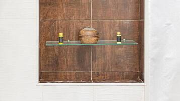 Ein Badezimmer mit einem Holzbadschrank, zwei Glasregalen und einer weiß gefliesten Wand.