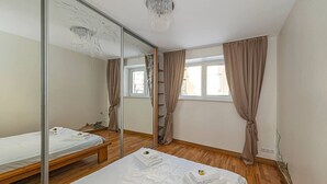 Quarto com piso de madeira, cama com roupa branca, espelho e janela com cortinas.