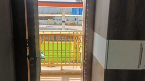 Un umbral abierto que da a un balcón con vistas a un campo deportivo y un edificio con detalles azules y naranjas.