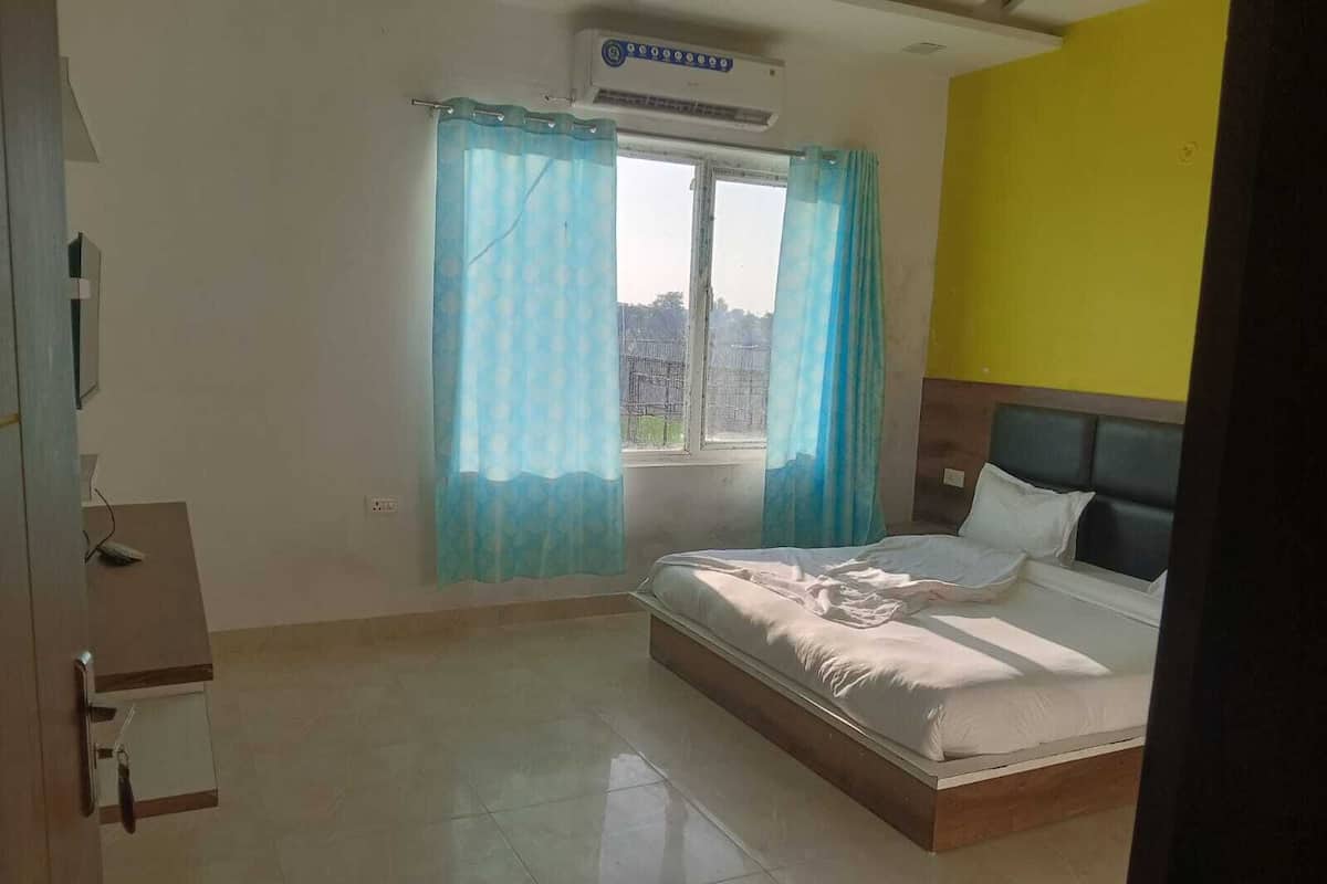 Quarto com cama, janela com cortinas, aparelho de ar condicionado e parede amarela.