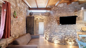 Habitació de parets de pedra amb un sofà, un televisor fixat a la paret i un sostre de fusta.