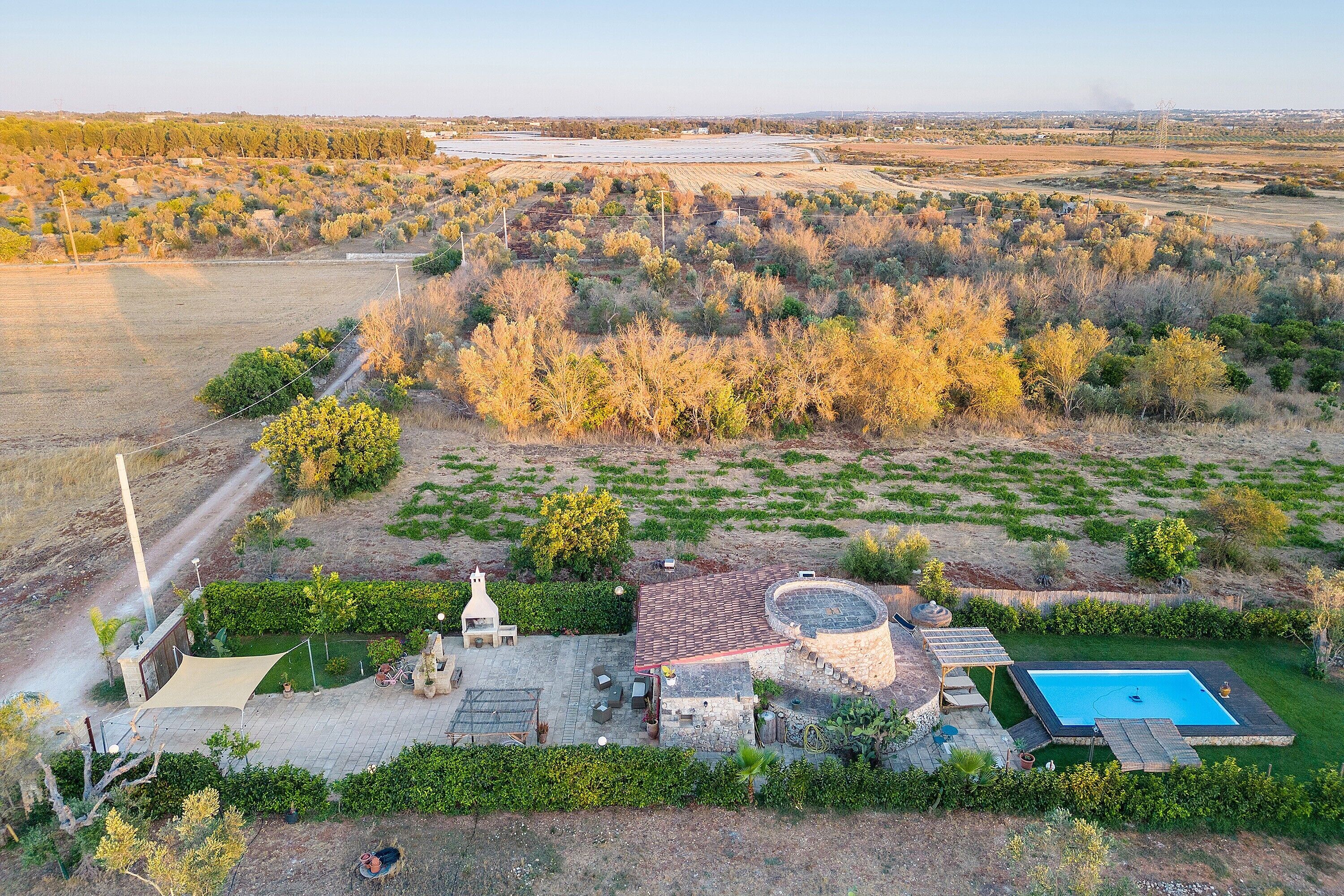 Vista aérea de una propiedad con piscina, zona de patio y un extenso campo al fondo.