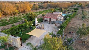 Una propietat rural amb una casa de pedra, mobiliari exterior, un pati ombrívol i vegetació als voltants.