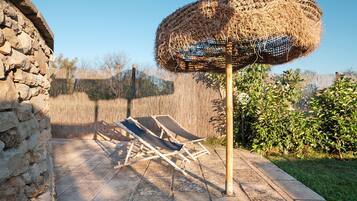 Un muro in pietra, un ombrellone di paglia e due poltrone su una terrazza.
