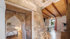 Un interior rústic de pedra amb un llit, zona de menjador i una llar de foc.