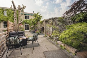 A patio with outdoor furniture, a stone wall, and a garden area. - Old Earth | Ridgestone (Kendal)