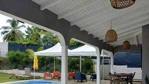 Een terras buiten met een zwembad, een witte pergola en zitplaatsen.