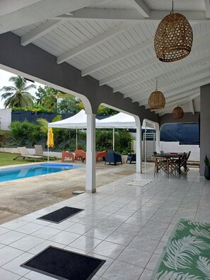 Ein Außenbereich mit Terrasse, Pool, weißem Pergola und Gartenmöbeln.