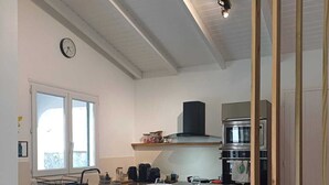 Een moderne keuken met een centraal eiland, een magnetron en een kookplaat. Er is een raam dat natuurlijk licht binnenlaat en een klok aan de muur.