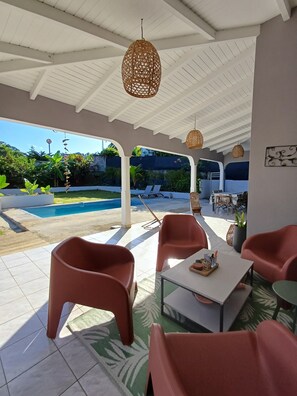 An outdoor patio area with modern furniture, a pool, and a view of the surrounding greenery. - Description (Lamentin)