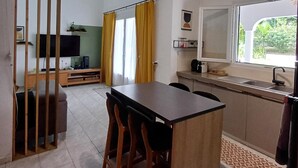 Een ruime woonkamer met een eettafel, stoelen, een televisie en een keuken met een spoelbak en raam.