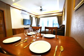 A dining area with a wooden table set for two, equipped with white plates, gold cutlery, and wine glasses. - Spacious Corner 1-bedroom Condo With 2 Balconies - Baan Suan Lalana (Pattaya)