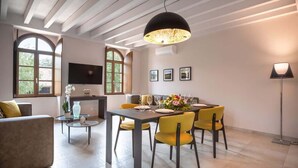 Un comedor con una mesa dispuesta para seis personas, rodeado de sillas amarillas, una lámpara colgante moderna y un sofá al frente.
