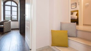 Un pasillo con una puerta que da a un dormitorio, una ventana y una escalera con un banco.