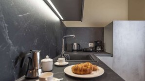 Cocina moderna con encimera de mármol oscuro, cafetera, hervidor, un croissant en un plato y una taza.