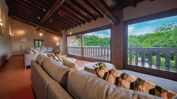 A spacious living area with a wooden ceiling, a large window with a balcony, and a sofa with patterned cushions. - Villa Diana - Private Villa with pool (Provincia di Brescia)